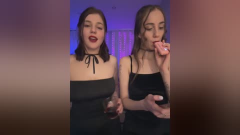 A video of two young women with pale skin, dark hair, and red lipstick, dressed in black strapless dresses, eating ice cream, set against a dimly lit background with purple and white hues.