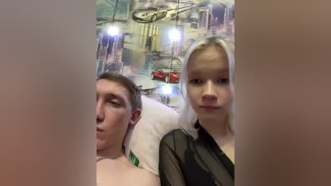 Video of a man and woman sitting closely, both with light skin and straight hair. The man is asleep, resting his head on the woman's shoulder. The background features a mural with a cityscape and a red car.