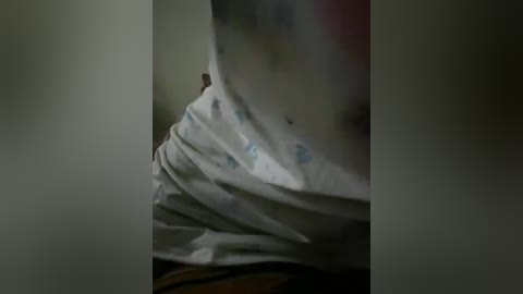 A close-up video of a person's upper body in a dimly lit room, showing a wrinkled white shirt with faint blue patterns, partially obscured by a dark, blurry background.