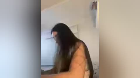 A blurry video of a young woman with long dark hair, wearing a green top, leaning over a table in a dimly lit room.