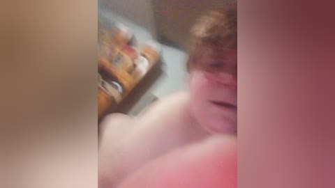 Blurry video of a young person with reddish hair, partially visible face, and a shirtless torso, taken in a dimly lit room with a wooden dresser in the background.