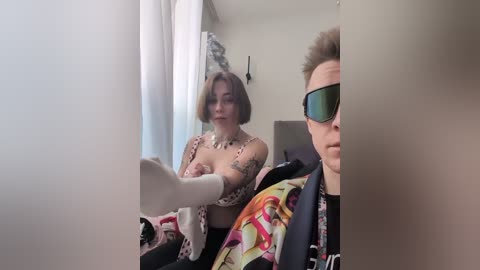 Video of a woman with a bob haircut, wearing a leopard print bikini top, and a man with a short hairstyle and sunglasses, sitting in a car.