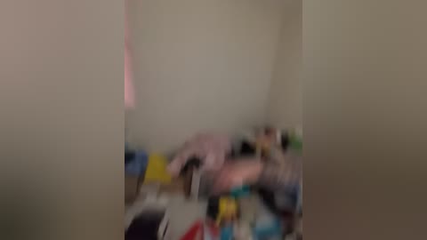 A blurry video of a messy bedroom with a pink and white bedspread, scattered toys, and a beige wall, creating a chaotic and disorganized atmosphere.
