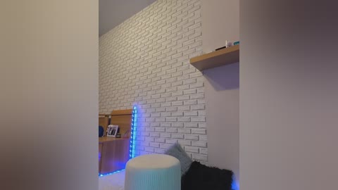 Video of a modern, minimalist bedroom with a white brick accent wall, wooden shelves, blue LED strip lighting, a black furry pillow, and a white, textured ottoman.