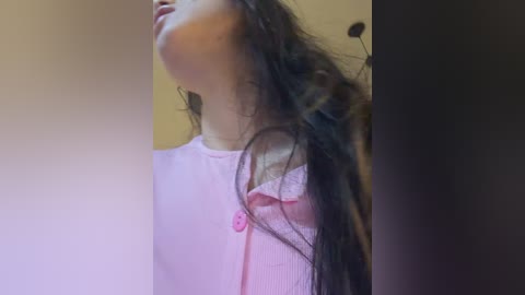 A video of a young woman with long, dark hair, wearing a light pink blouse, captured from a low angle, with blurred background.