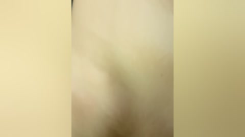 Video of a naked person standing with their back to the camera, showing a smooth, light skin tone. The background is a plain beige wall, creating a simple, unembellished setting. The image lacks details, focusing on the overall shape and texture of the skin.
