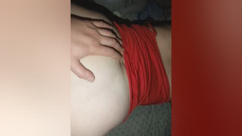Video of a light-skinned person's lower body in a red tank top, with a hand resting on their buttocks, on a carpeted floor, red filter applied.