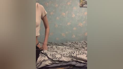 A video showing a woman in a white blouse kneeling on a bed with a leopard-print duvet, partially obscured by a wall with a floral wallpaper pattern.