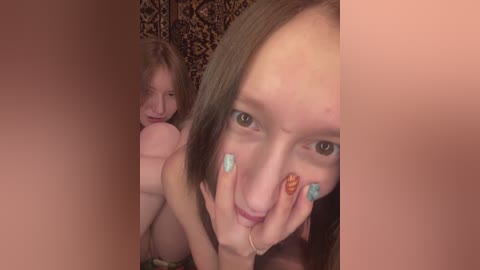 Video of a young woman with fair skin, green eyes, and straight brown hair, wearing teal nail polish, looking up and touching her nose. Behind her, another woman with similar features is visible. Background features leopard print.