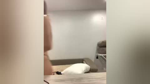 A video of a dimly lit bedroom with a white pillow on the floor and a grey couch in the background. The room's walls are painted light grey.