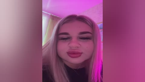 Video of a young woman with long blonde hair, fair skin, and pink lips, making a pouty face. Background features a colorful, blurred room with purple lighting.
