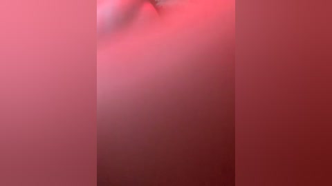 A blurred, close-up video of a person with light skin and medium-length hair, captured in a reddish-pink hue, standing in a dimly lit room. The image is soft and out-of-focus, emphasizing the background's warm tones.