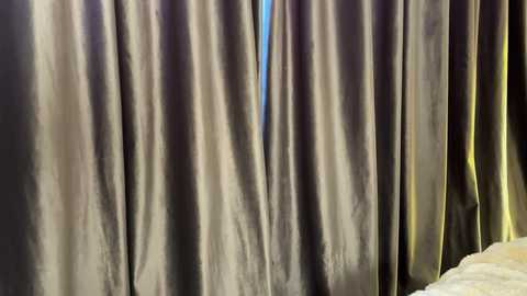 Video of a dark, shiny curtain with a slight sheen, partially revealing a blue sky behind it, suggesting an outdoor setting.