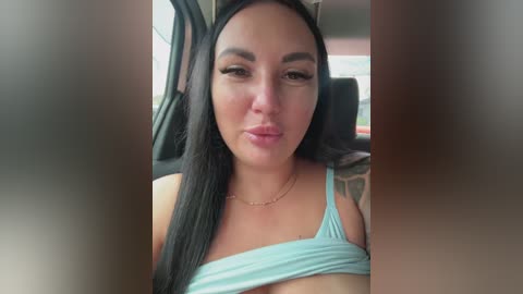 Video of a Latina woman with long black hair, wearing a turquoise tank top, sitting in a car. She has a tattoo on her left arm.