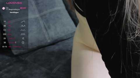 A video shows a close-up of a person with long, dark hair, wearing a black shirt, kneeling on a grey couch. A video game overlay displays \"LOVE2CUBE\" and \"messaging.\