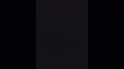 A dark, black-and-white video of a vertical rectangle against a pitch-black background, with faint, indistinguishable details suggesting a textured, possibly fabric material. The image is minimalistic and abstract, with no discernible objects or people.