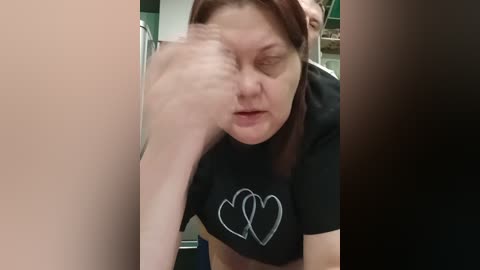 Video of a middle-aged woman with fair skin, light brown hair, wearing a black T-shirt with a white heart design, in a blurred motion, possibly from a fast movement.