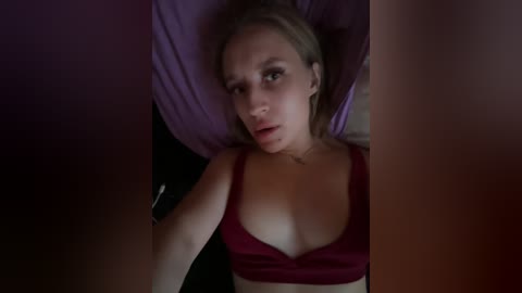 Video of a young Caucasian woman with light skin, brown hair, wearing a red bra, lying on a purple pillow, looking worried.