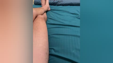 Video of a person lying on a teal bed, with a light-skinned hand reaching out, fingers curled, suggesting a moment of relaxation or contemplation.