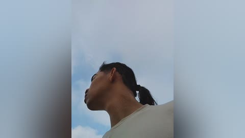 A video of a woman with short dark hair in a ponytail, wearing glasses and a white shirt, looking upward against a cloudy sky. The image is slightly blurred, emphasizing depth.