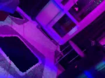 A video of a dimly lit, indoor scene with neon purple and blue lighting, featuring a white wall, a darkened doorway, and a partially visible figure.