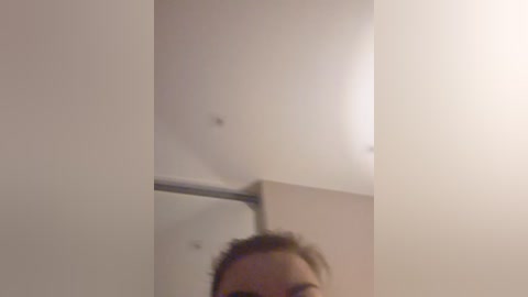 A video of a woman with light skin and shoulder-length brown hair partially visible, standing in a dimly lit bathroom with beige walls and a metallic shower rod.