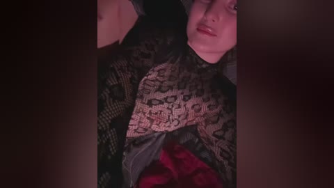 A close-up video of a woman with fair skin, wearing a black lace top and red lace underwear, lying on a dark background, with her arms raised above her head.