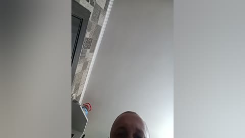 Video of a ceiling corner with a white plasterboard wall and a grey tiled edge. A partially visible person's head is below the tiles, with a light complexion and short hair.