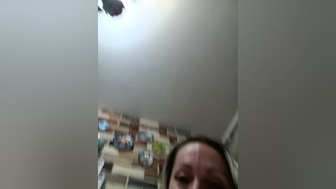 A video of a ceiling with a bright light source and blurred tiles, showing the edge of a person's face, with a casual, slightly out-of-focus style.