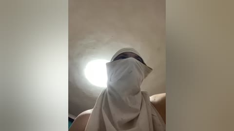 Video of a person wearing a white surgical mask, standing in a dimly lit room with a circular light source in the background, creating a halo effect.