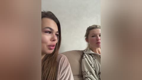 Video of two young women, one with long brown hair in a light pink sweater, the other with blonde hair in a gray hoodie, both looking slightly to the right.