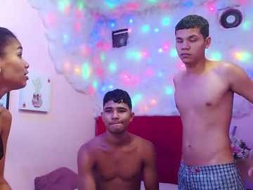 Video of three shirtless young men in a colorful, festive room with fairy lights. One man stands, another sits, and the third is on the left.