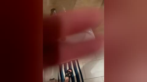 A video showing a person with dark skin, possibly of African descent, sitting on a blue and white striped towel on a tiled floor. The image is partially obscured by a red curtain.