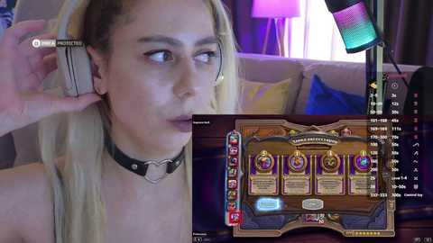 Video of a woman with long blonde hair wearing a black choker, playing a slot machine game on her phone, set in a dimly lit room with purple lighting and a lamp.