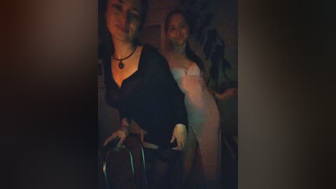A dimly lit video features two women, one in black lingerie and the other in a sheer nightgown, standing close together.