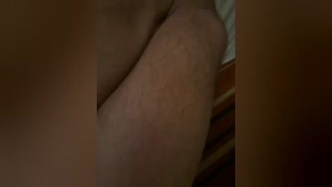 Video of a close-up of a pale, smooth-skinned thigh with faint hair, partially covered by a beige garment, and a wooden surface in the background.