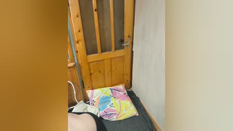 A video of a narrow hallway with a wooden door featuring frosted glass panels. A colorful, patterned gift bag is on the floor, and a person's arm is partially visible in a black shirt, holding a white box.